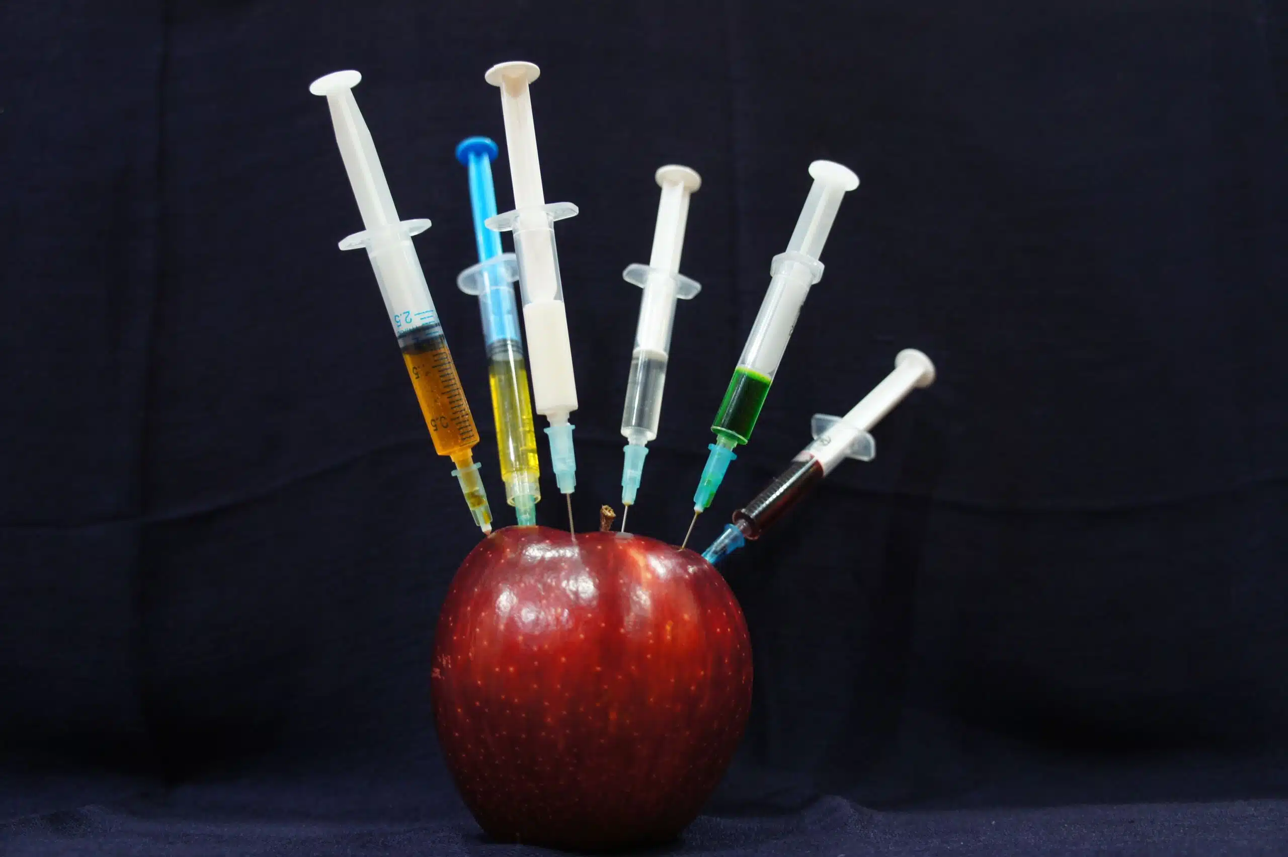 An apple with syringes stuck in it