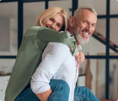 Man with greying hair gives women piggyback while both smile